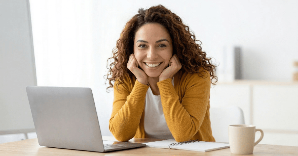 A smiling woman in a mustard-yellow cardigan sits at a desk with a laptop and notebook, symbolizing a confident beginner blogger starting their step-by-step roadmap.